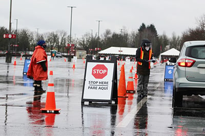 From left, April Cuprill-Comas, OHSU's executive vice president and general counsel, and OHSU research associate Kaylyn Devlin direct traffic on Sunday, Jan. 24 at a drive-through vaccination clinic at Portland International Airport. OHSU is collaborating with the Port of Portland and the American Red Cross to operate the site. (Photo Credit: OHSU/Erik Robinson)